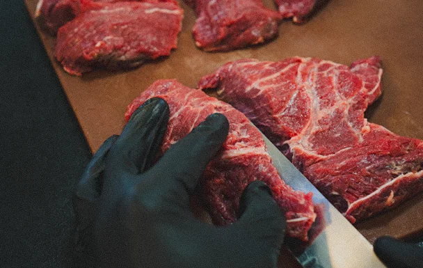 Mains gantées coupant un morceau de viande rouge.